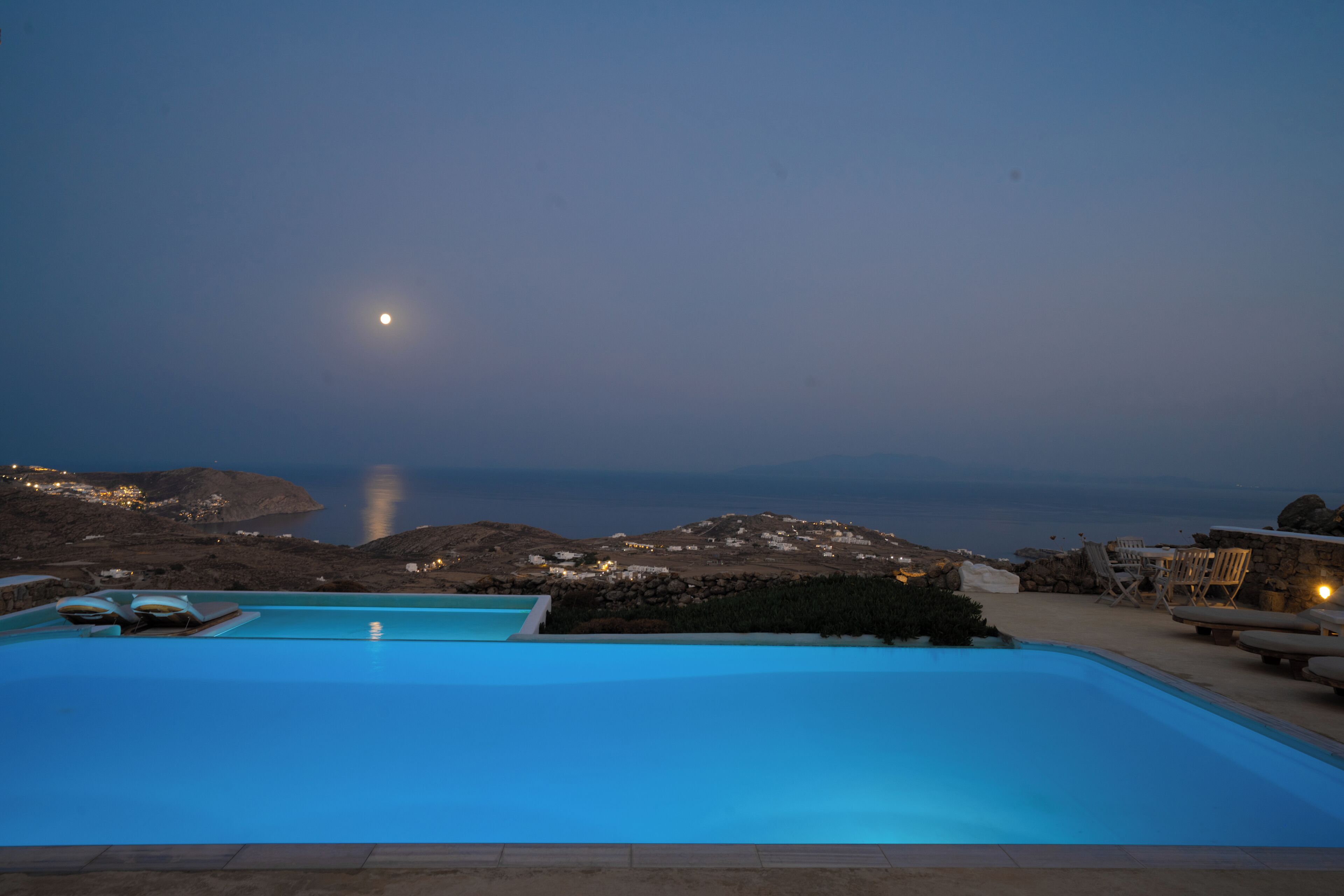 Una piscina con vista sul mare e le colline al tramonto.