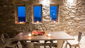 A stone-walled room with a wooden table set for dining, candles, and a view through windows. - Amallini Suites Mykonos (Mykonos)
