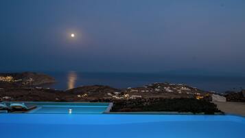 A poolside view with a moonlit night, rocky terrain, and distant buildings.