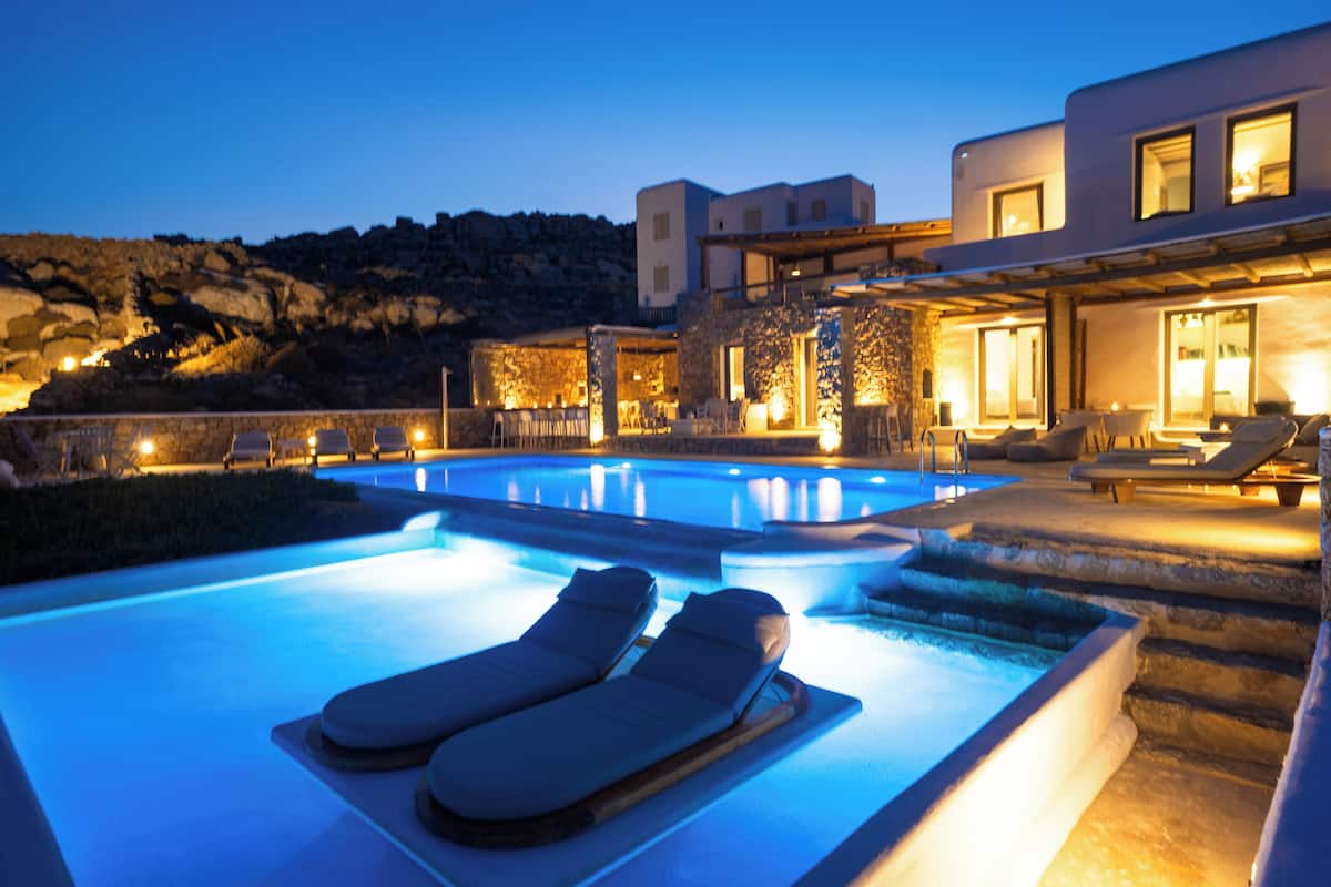 Una piscina con sillones de descanso, un muro de piedra y un edificio moderno con amplias ventanas.