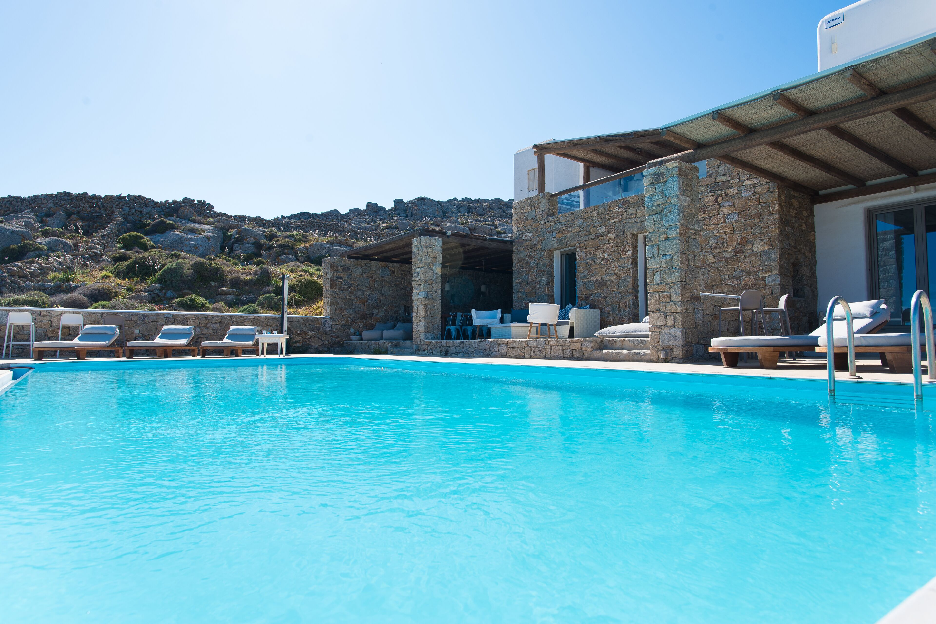 Ein Pool mit Liegestühlen, Steinmauern und Blick auf die Hügel.