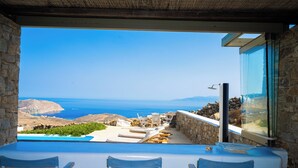 A terrace with a view of the sea, stone walls, and lounge chairs. - Amallini Suites Mykonos (Mykonos)