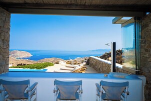 A terrace with a view of the sea, stone walls, and lounge chairs.