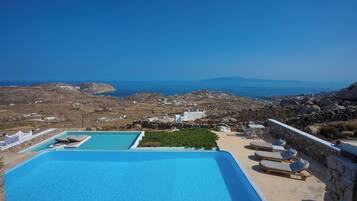 Un espace piscine doté de chaises longues et offrant une vue sur la mer et le paysage.