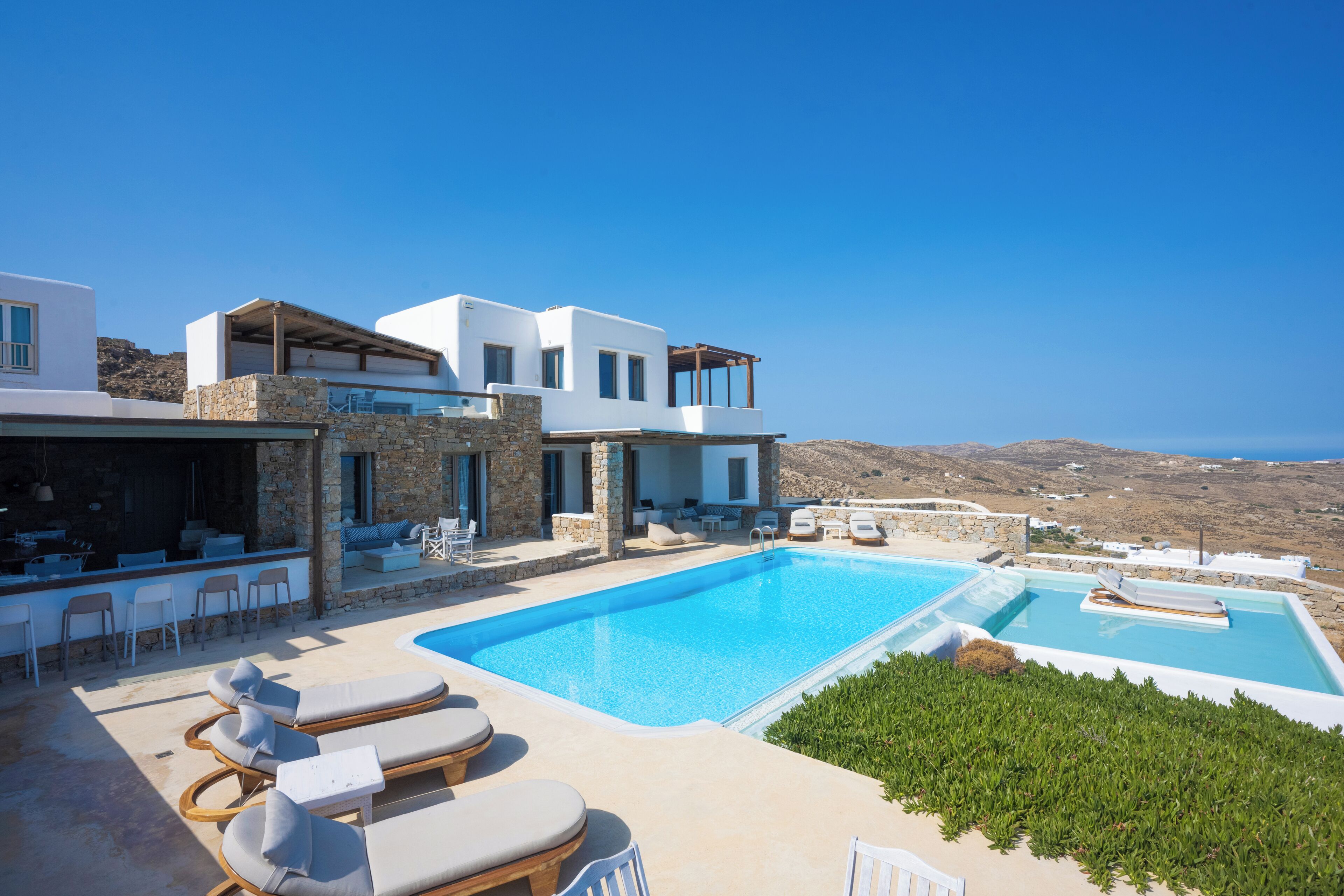 Eine moderne Villa mit großem Swimmingpool, Sitzgelegenheit im Freien und Blick auf die Landschaft.