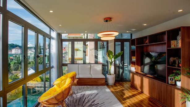 A modern living room with a large window, a sofa, a television, and a wooden bookshelf. - Tan Villa 2 (Xuan Huong - Da Lat)
