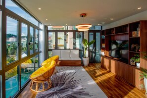 A modern living room with a large window, a sofa, a television, and a wooden bookshelf. - Tan Villa 2 (Xuan Huong - Da Lat)