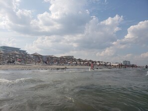A beach with umbrellas and lounge chairs, a sandy shore, and buildings in the background. - Apartment Summerland Mamaia (Constanta)