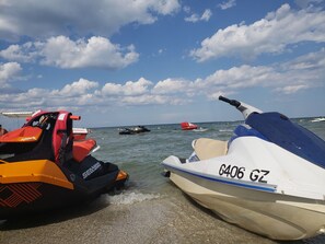 Ein Jetski und ein Boot liegen an einem Strand bei blauem Himmel und ruhiger See.