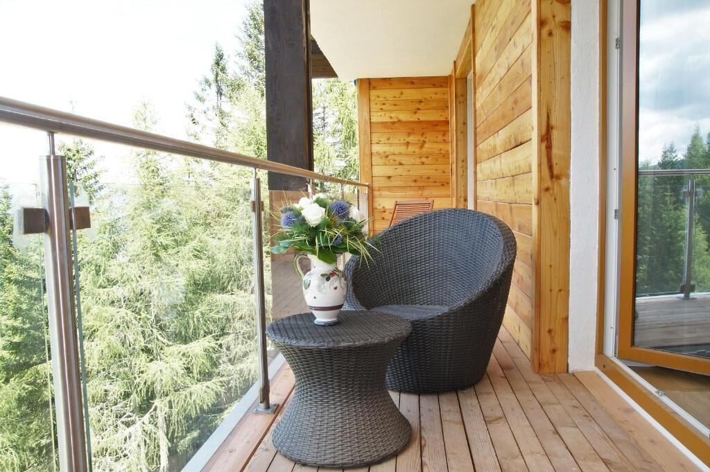 A balcony with wicker furniture, a vase with flowers, and a view of trees.