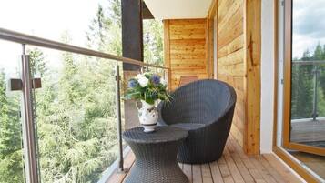 A balcony with wicker furniture, a vase with flowers, and a view of trees.