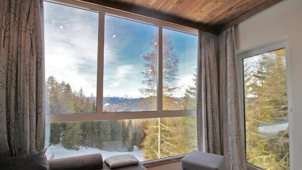 A room with a large window offering a view of a snowy landscape and trees. There is a sofa and a chair inside the room. - Alpengasthof Krische (Sankt Georgen am Kreischberg)