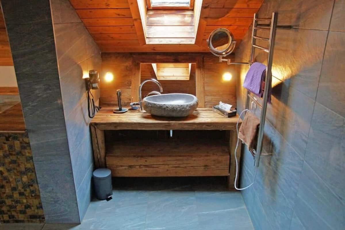 Ein kleines Badezimmer mit Oberlicht, Holzwaschtisch, Steinbecken und einer kleinen Mülltonne.