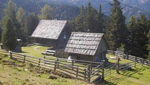 A rustic cabin with a sloped roof, surrounded by a wooden fence, set against a backdrop of dense forest and mountains. - Alpengasthof Krische (Sankt Georgen am Kreischberg)