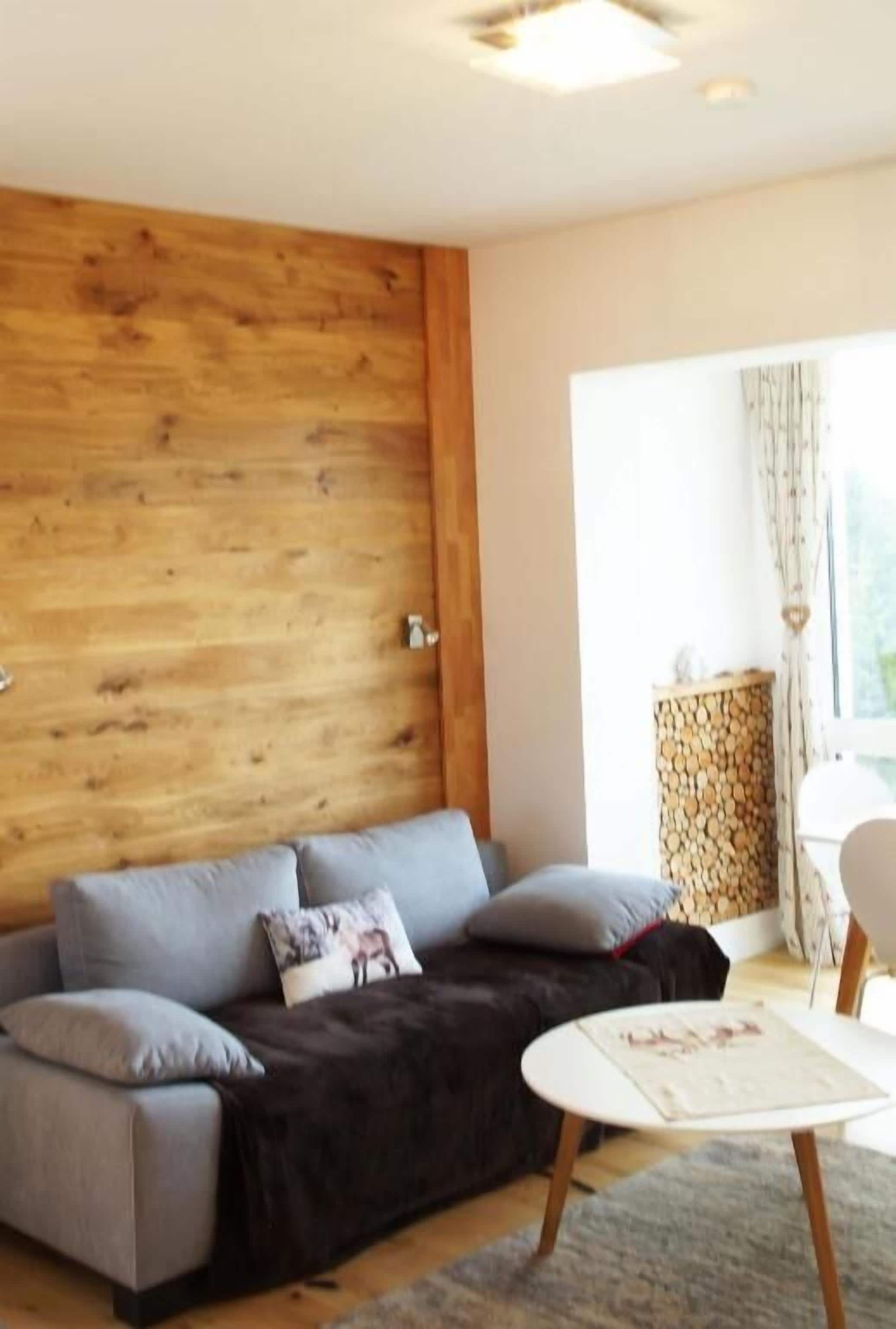 Un salon moderne avec un mur d’accent en bois, un canapé gris, une petite table ronde et une fenêtre avec des rideaux.