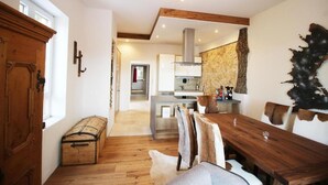 A modern kitchen with a stone backsplash, wooden ceiling beams, and a dining area with a wooden table and chairs. - Alpengasthof Krische (Sankt Georgen am Kreischberg)