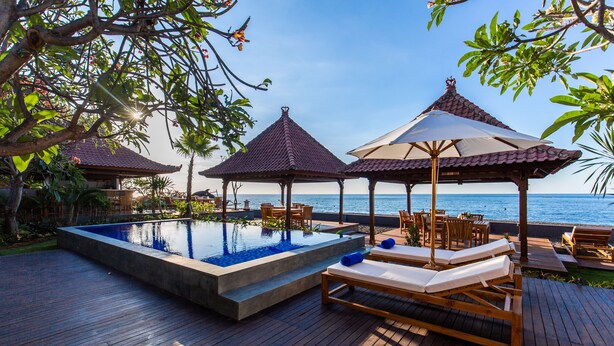 A wooden deck with a swimming pool, lounge chairs, and umbrellas overlooking the sea. - Nalika Beach Resort & Restaurant - Adults Only (Seririt)