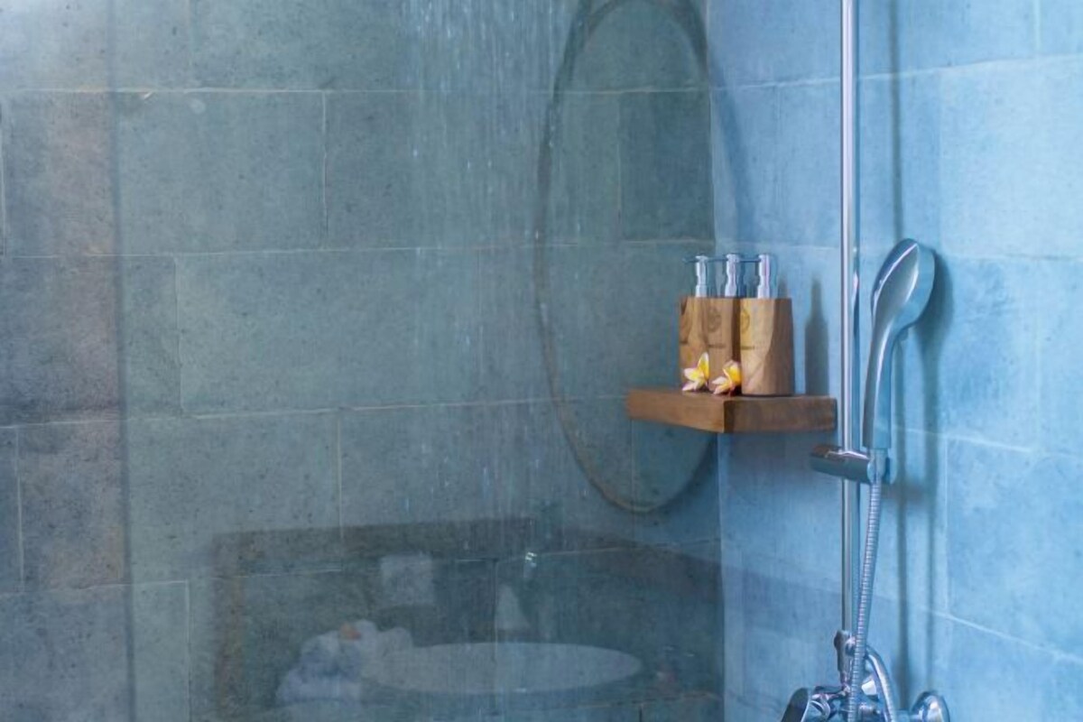 A shower area with a glass door, a wooden shelf with toiletries, and a metal showerhead.