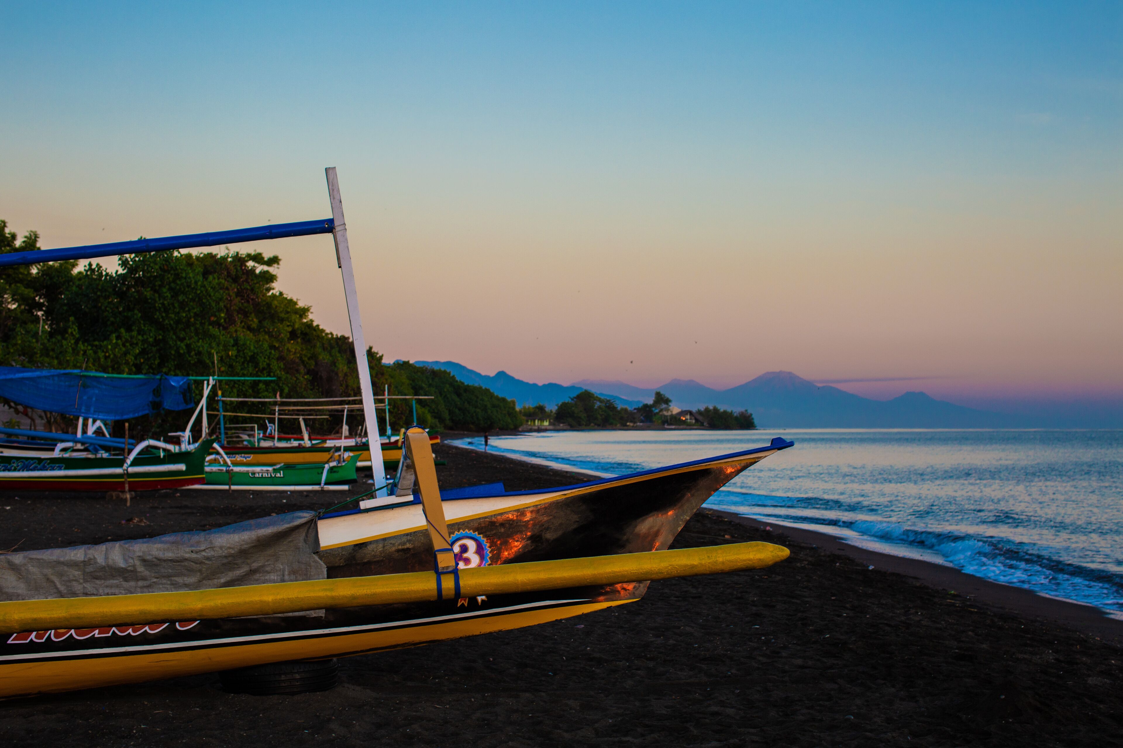 Una playa con barcos y montañas al fondo.
