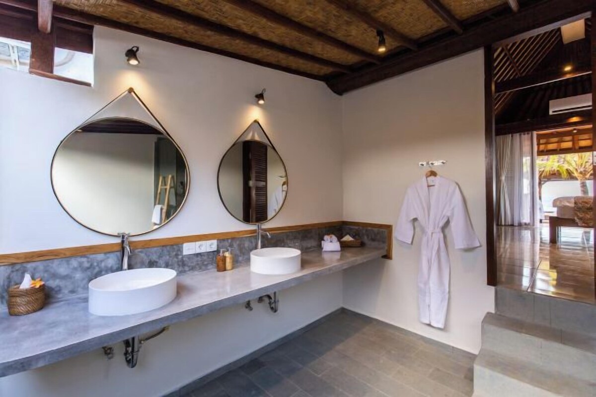 A bathroom with two sinks, a large mirror, and a robe hanging on the wall.