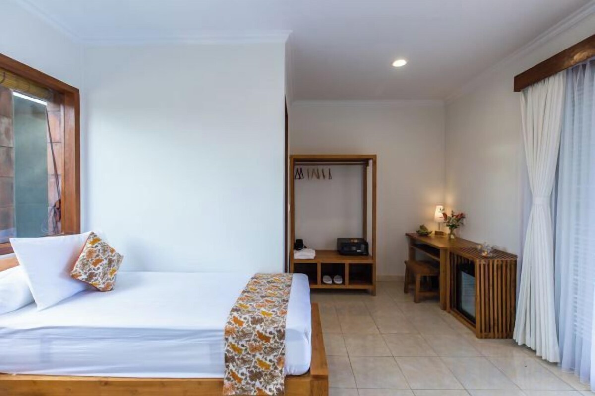 Habitació d'hotel amb un llit, una taula de nit amb una làmpada, una zona de seients petita i un armari.