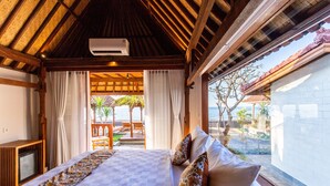 A hotel room with a checkered bedspread, a wooden ceiling, and a view of the beach. - Nalika Beach Resort & Restaurant - Adults Only (Seririt)