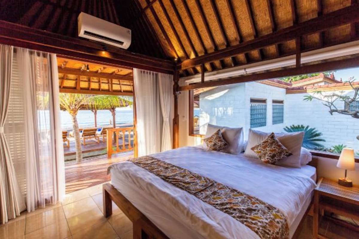 A bedroom with a large bed, a view of the beach, and a balcony with a table and chairs.