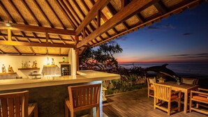 A wooden deck with a bar area, chairs, and a view of the ocean at sunset. - Nalika Beach Resort & Restaurant - Adults Only (Seririt)