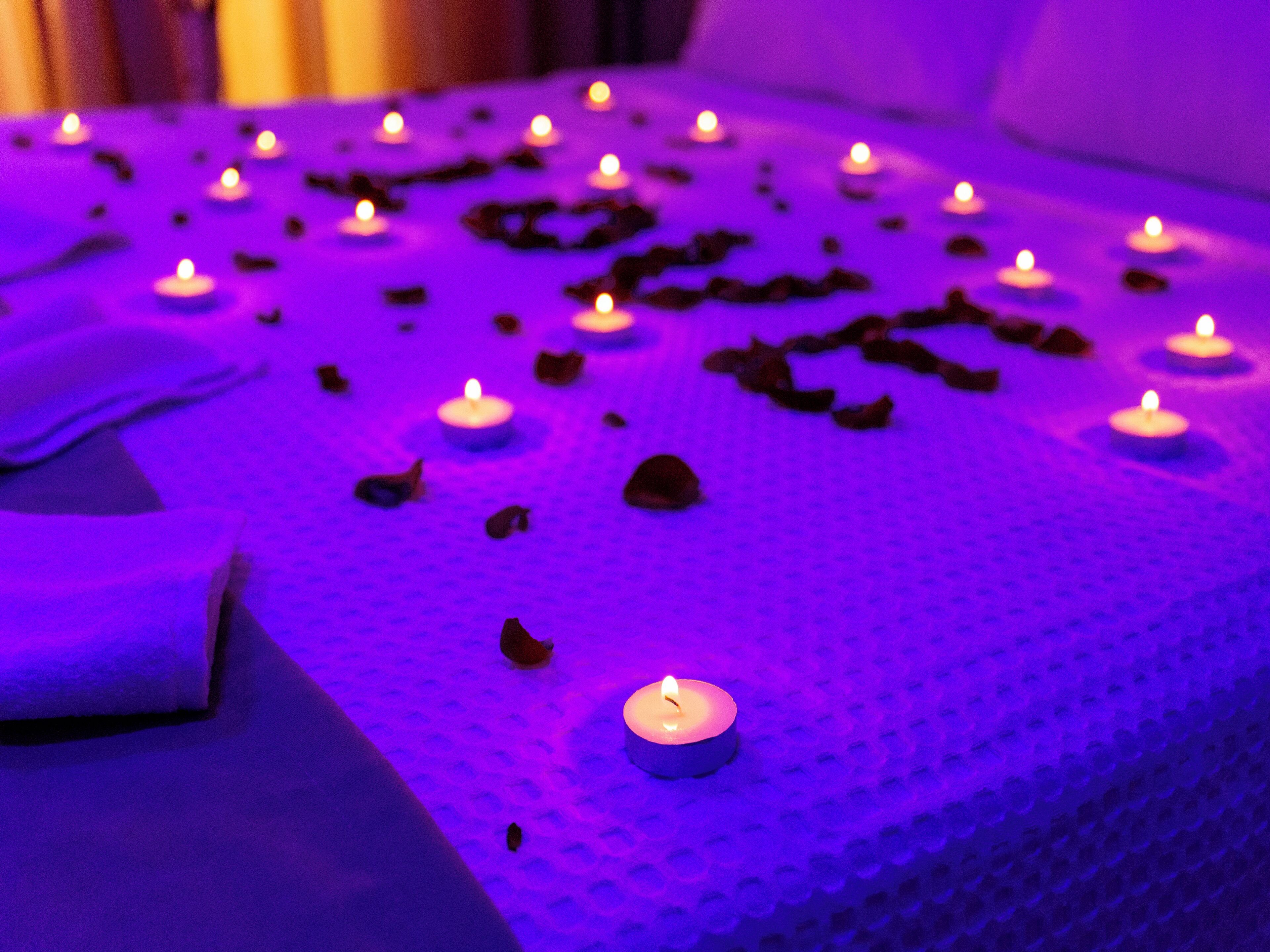 A bed with multiple lit candles and scattered rose petals.