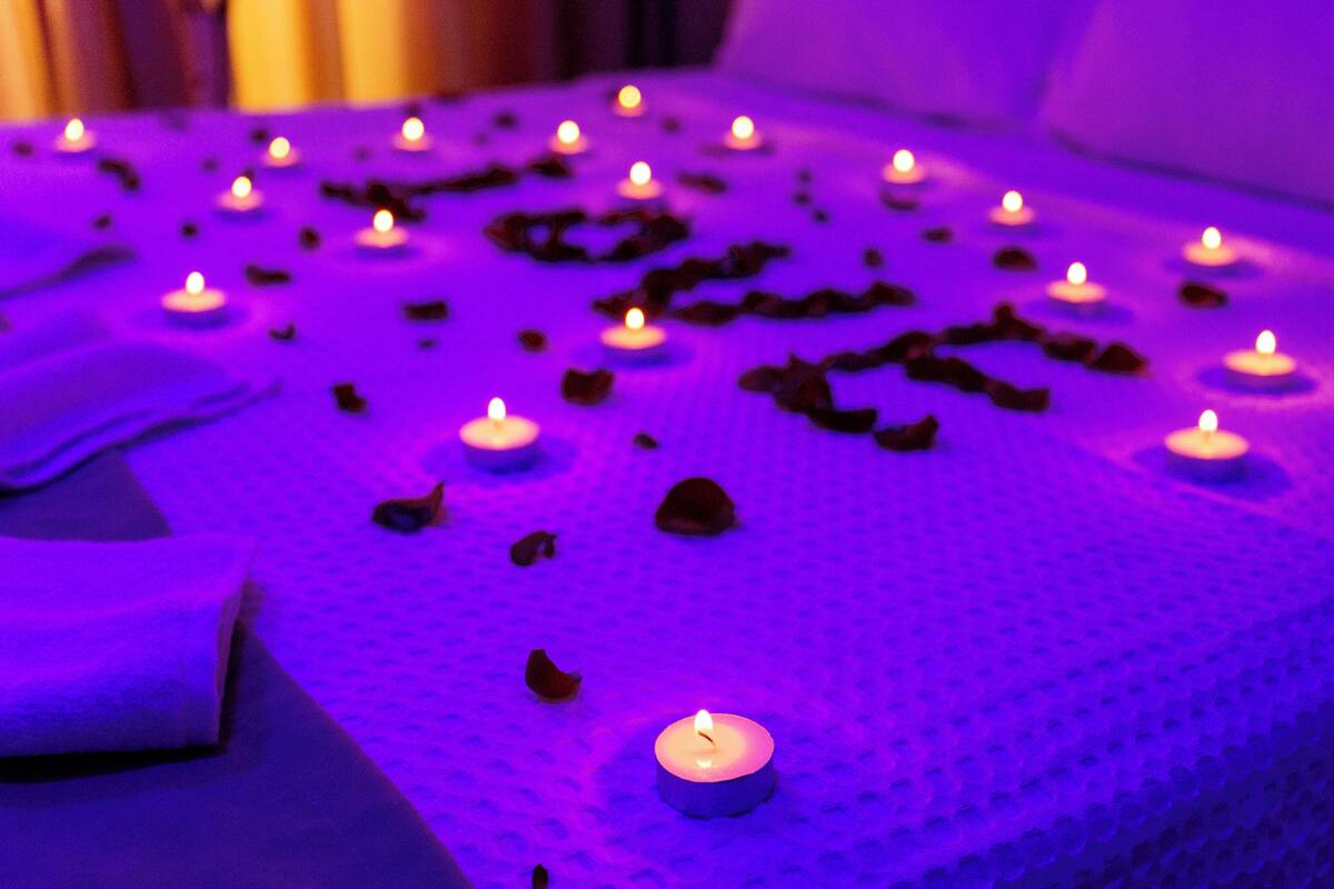 A bed with multiple lit candles and scattered rose petals.