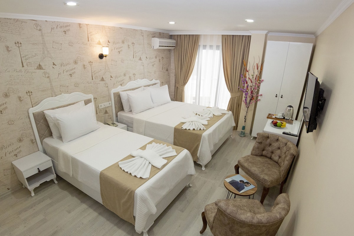 A hotel room with two beds, a sitting area with a chair, a small table, and a wardrobe.