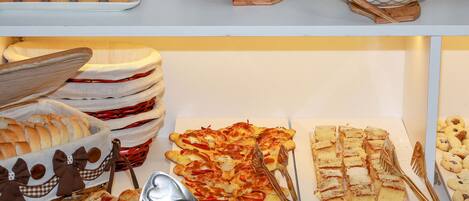Un buffet proposant une variété de plats, notamment du pain, des viennoiseries et des desserts.