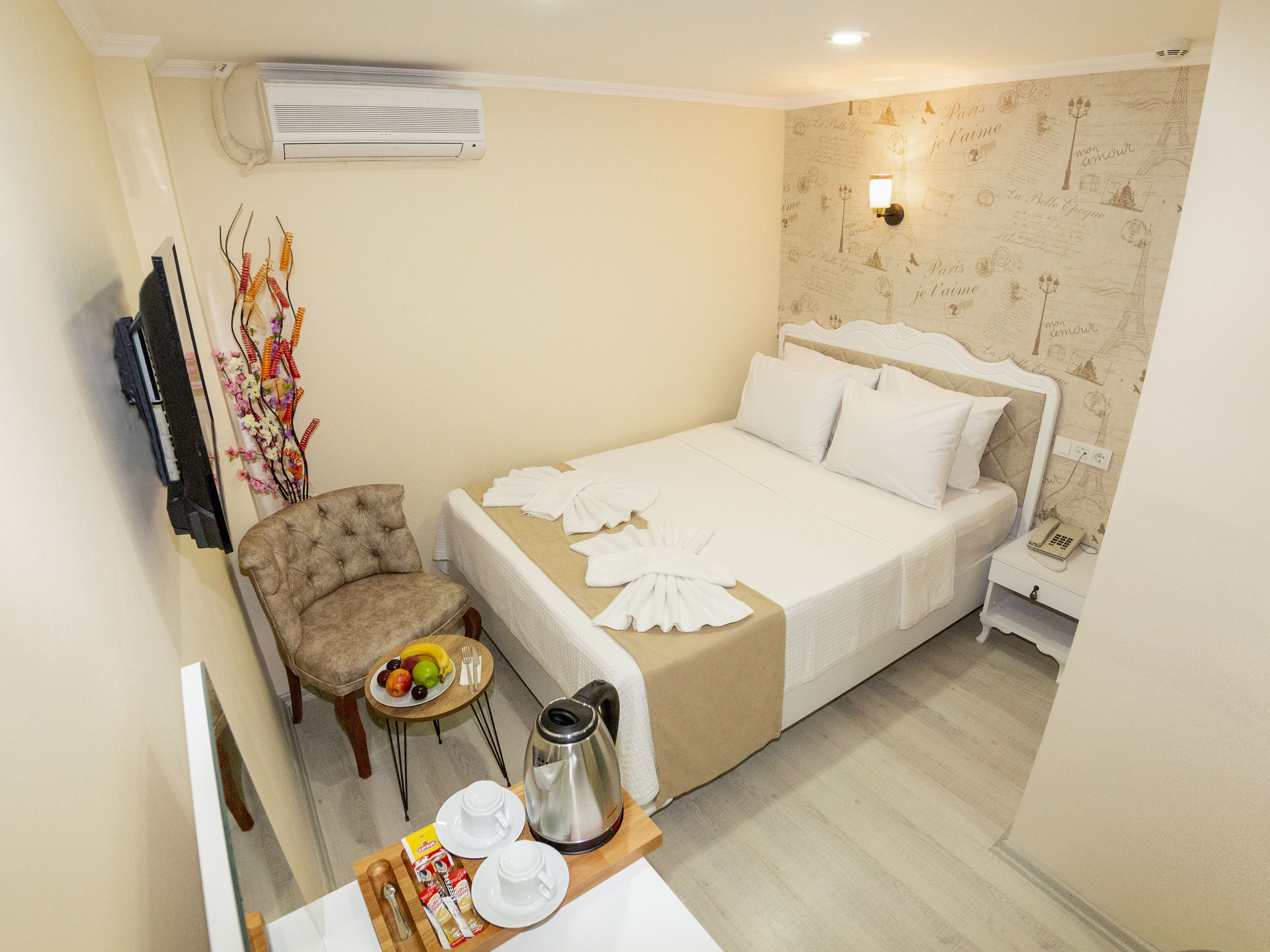 A hotel room with a bed, a chair, a small table with breakfast items, and a wall-mounted air conditioner.