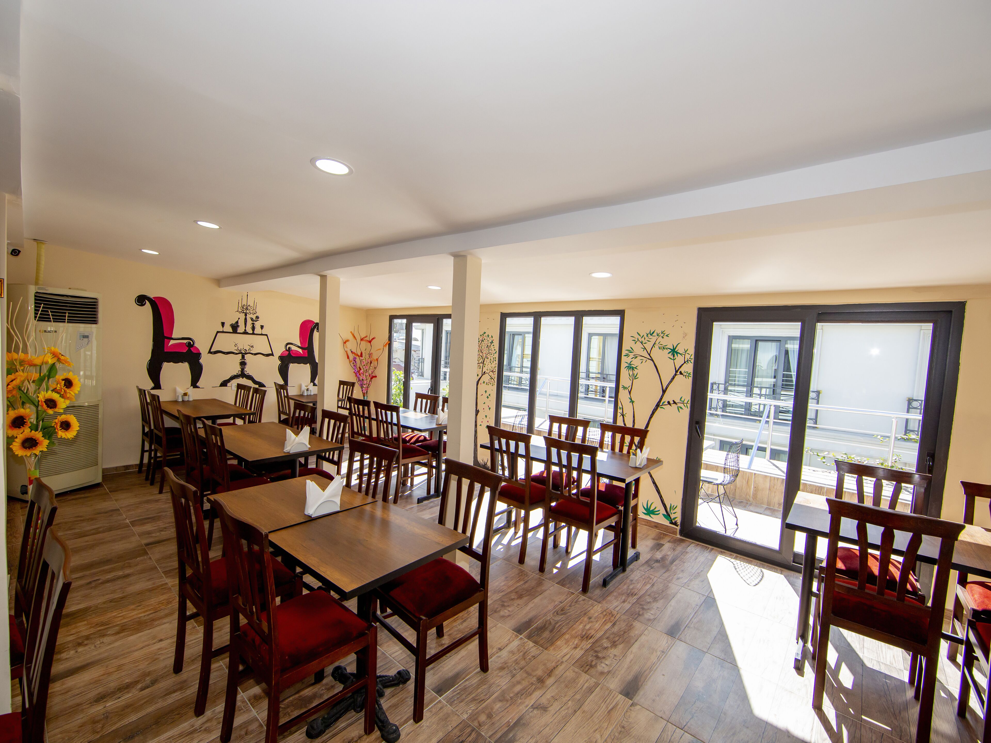 A spacious dining area with wooden tables and chairs, large windows offering a view of the outside, and decorative wall art.