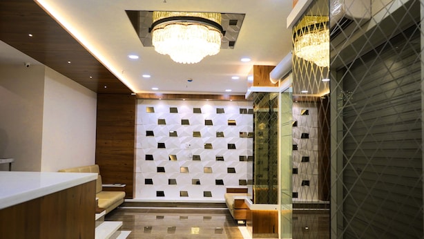 A modern reception area with a wooden reception desk, a seating area with a sofa, a patterned wall, and a glass partition. - Hotel Royal Treat (Surat)