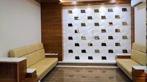 A modern waiting area with two beige sofas, a wooden accent wall, and a patterned wall with mirrors. - Hotel Royal Treat (Surat)