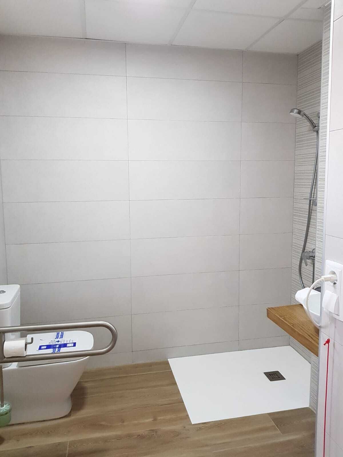 Een kleine, schone badkamer met witte tegels, een houten vloer, een toilet en een douche.