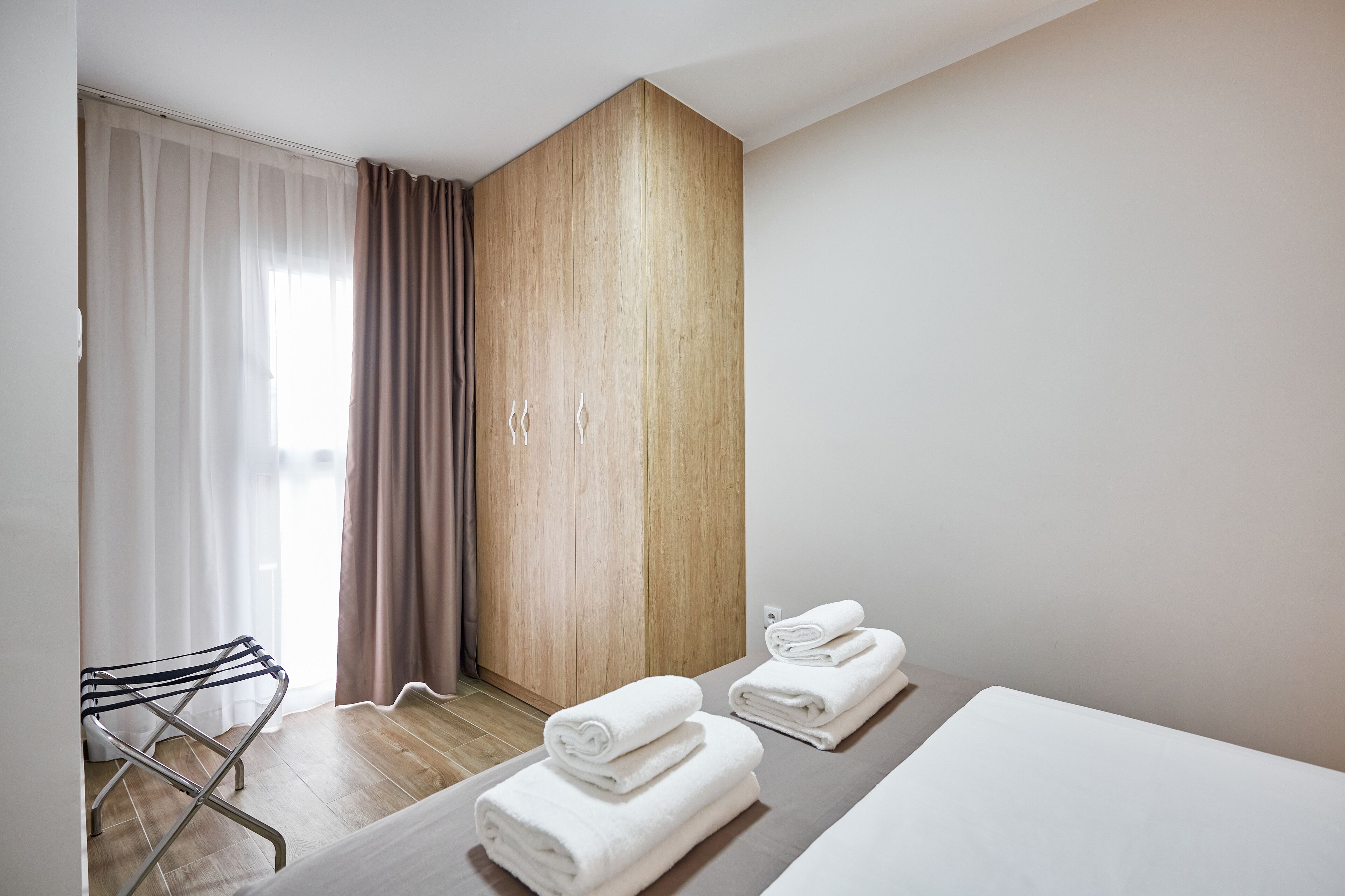 A hotel room with a wooden wardrobe, a drying rack, and neatly folded towels on the bed.