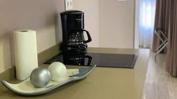 Una cafetera, un rollo de papel higiénico y dos objetos esféricos sobre una bandeja en una habitación con suelo y paredes color beige.