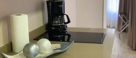 A coffee maker, a roll of toilet paper, and two spherical objects on a tray in a room with a beige floor and walls.