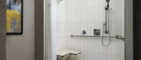 A modern shower area with a handheld showerhead, a wall-mounted control panel, and a small shelf.