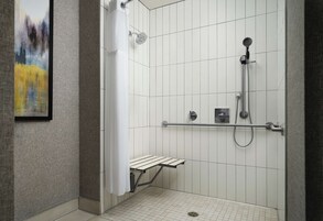 Un área de ducha moderna con cabezal de ducha de mano, panel de control en la pared y un pequeño estante.
