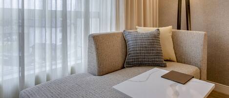 Habitación de hotel con sofá, mesa, lámpara y cortinas translúcidas.