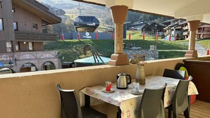 Een balkon met een tafel voor twee, met uitzicht op een bergachtig landschap met een skilift en chalets.