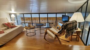 Een moderne woonkamer met een bank, een houten stoel, een klein rond tafeltje en een televisie.