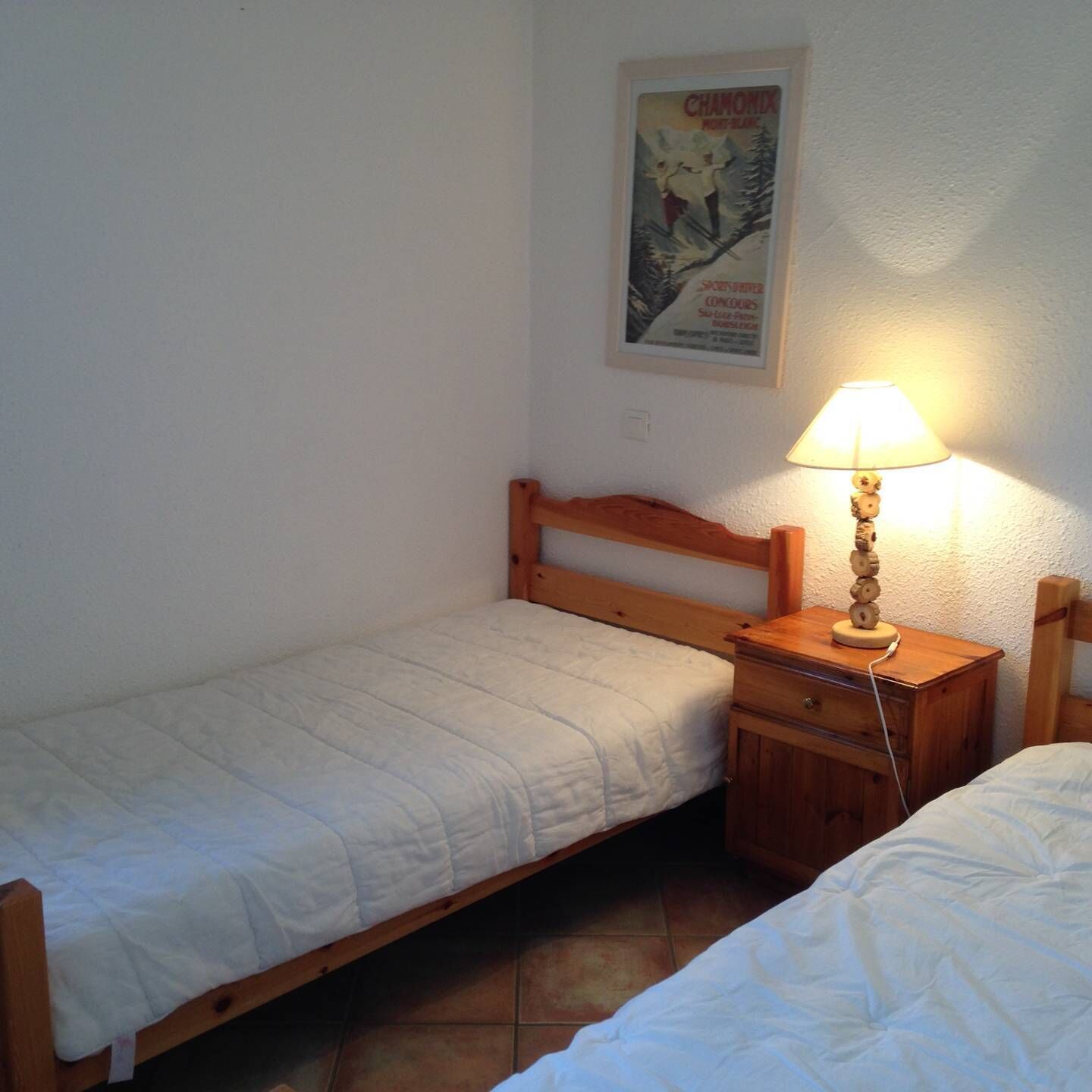Une petite chambre avec un lit simple, une tête de lit en bois, une table de chevet avec une lampe et une affiche accrochée au mur.