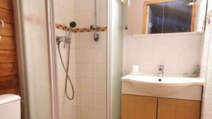 Een badkamer met een douchecabine van glas, een wit wastafelmeubel en houten kastjes.