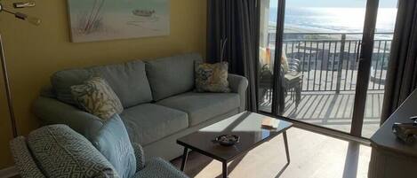 A living room with a sofa, armchair, and coffee table. There is a painting of a beach scene on the wall.