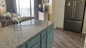Una cocina con encimera de granito, gabinetes color turquesa y un refrigerador de acero inoxidable.