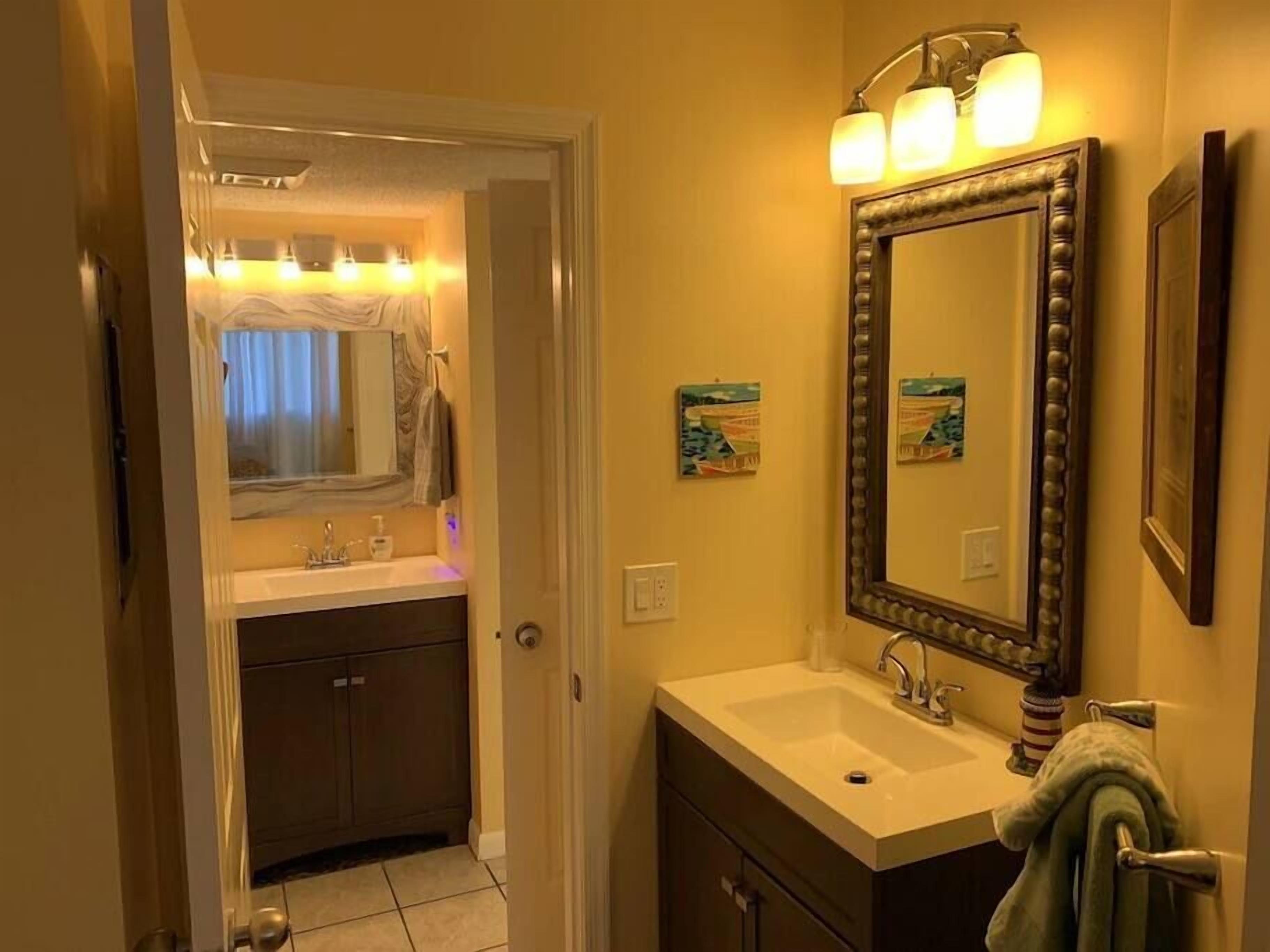 A bathroom with a vanity, sink, and mirror. There is a door leading to another room.